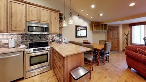 A kitchen with wooden cabinets, stainless steel appliances, a tiled backsplash, and a dining area with a wooden table and chairs. - Terracehouse - Steps to Slopes | Inviting Mountain Retreat, Pool & Hot Tub (Snowmass Village)