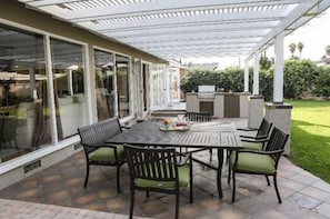 A covered patio with a table and chairs, a grill, and a glass door leading to a garden.