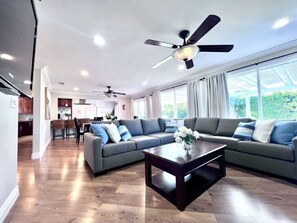 A modern living room with a sectional sofa, a coffee table, ceiling fans, and large windows.