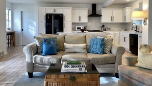 A modern living room with a sofa, coffee table, and a kitchen area with white cabinets and appliances. - Granbury Lake Rustic Retreat on Quiet Cove (Granbury)