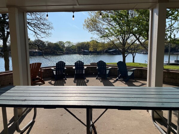Un espacio de estar al aire libre cubierto con vistas a un lago, con una mesa y varias sillas Adirondack.