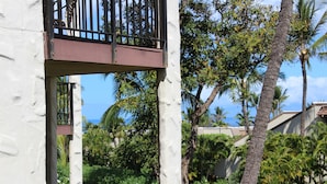 Een balkon met een metalen hek, omgeven door weelderige begroeiing en palmbomen.