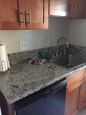 A kitchen with granite countertops, a stainless steel sink, wooden cabinets, and a dishwasher. - Tastefully upgraded. One of the only resort units with a full size laundry team. (Kihei)