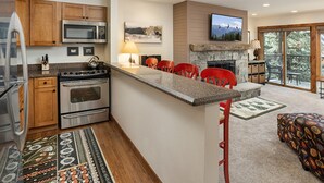 Une cuisine moderne avec des meubles en bois, des appareils électroménagers en acier inoxydable et un îlot central agrémenté de chaises rouges.