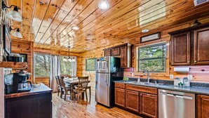 A wooden cabin interior with a kitchen, dining area, and large windows. - Cabin w/ Indoor Pool, Hot Tub, Sauna, Fire Pit (Sevierville)