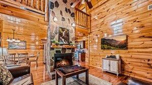 Een gezellig interieur van een chalet met een stenen openhaard, houten wanden, een eethoek en een woonkamer met lederen meubels.
