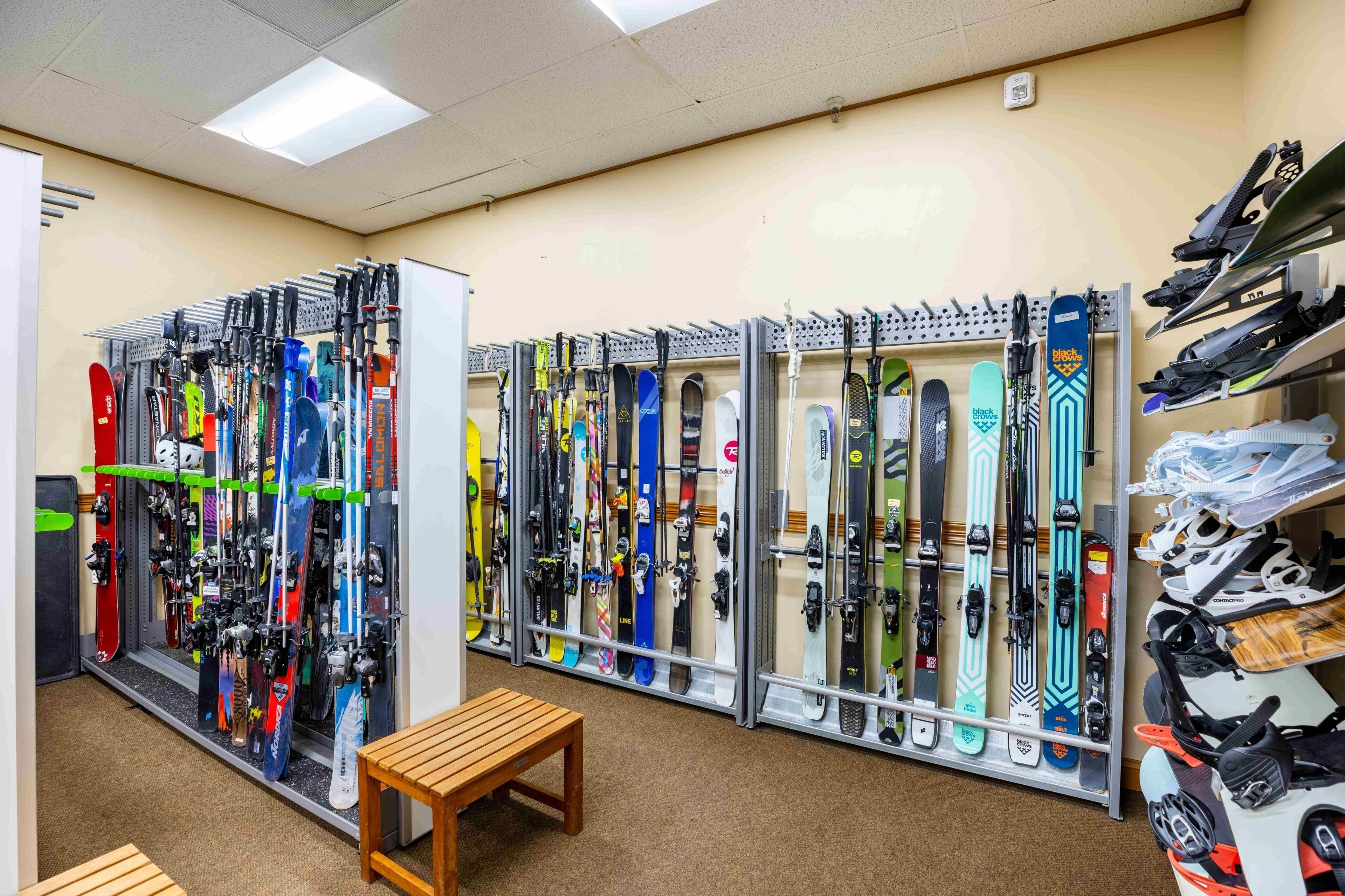 A ski rental shop with rows of skis and snowboards on racks, a wooden bench, and a shoe display.