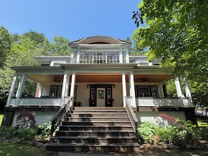 A two-story house with a front porch, steps leading to the entrance, and a garden area with plants and a small tree.
