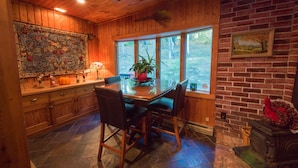 A wooden interior with a dining table, chairs, a fireplace, and a large window.