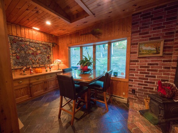 A wooden interior with a dining table, chairs, a fireplace, and a large window.