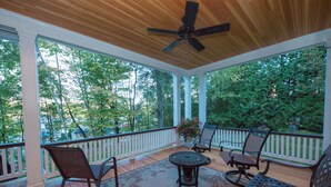 A covered porch with wooden flooring, white railings, and a ceiling fan. There are several chairs and a table with a floral table runner.