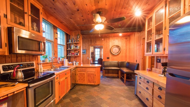 A kitchen with wooden cabinets, a microwave, stove, refrigerator, and a dining area with a bench.