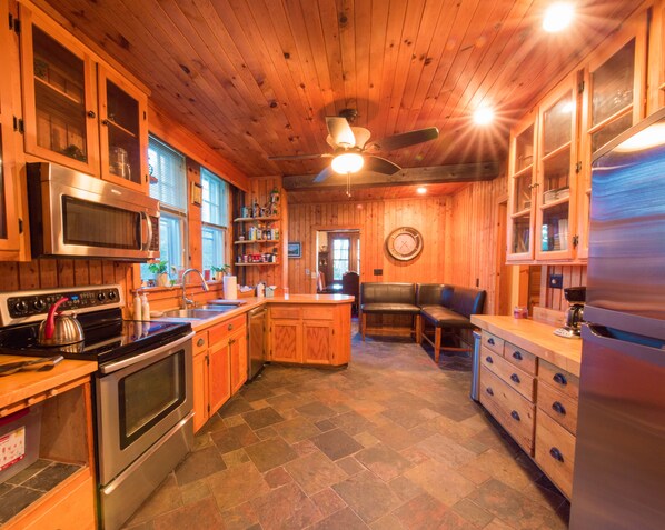 Una cocina con armarios de madera, microondas, estufa, refrigerador y un comedor con banco.