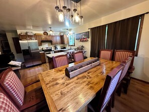 A kitchen with wooden cabinets, a refrigerator, a stove, and a dining area with a wooden table and checkered chairs.
