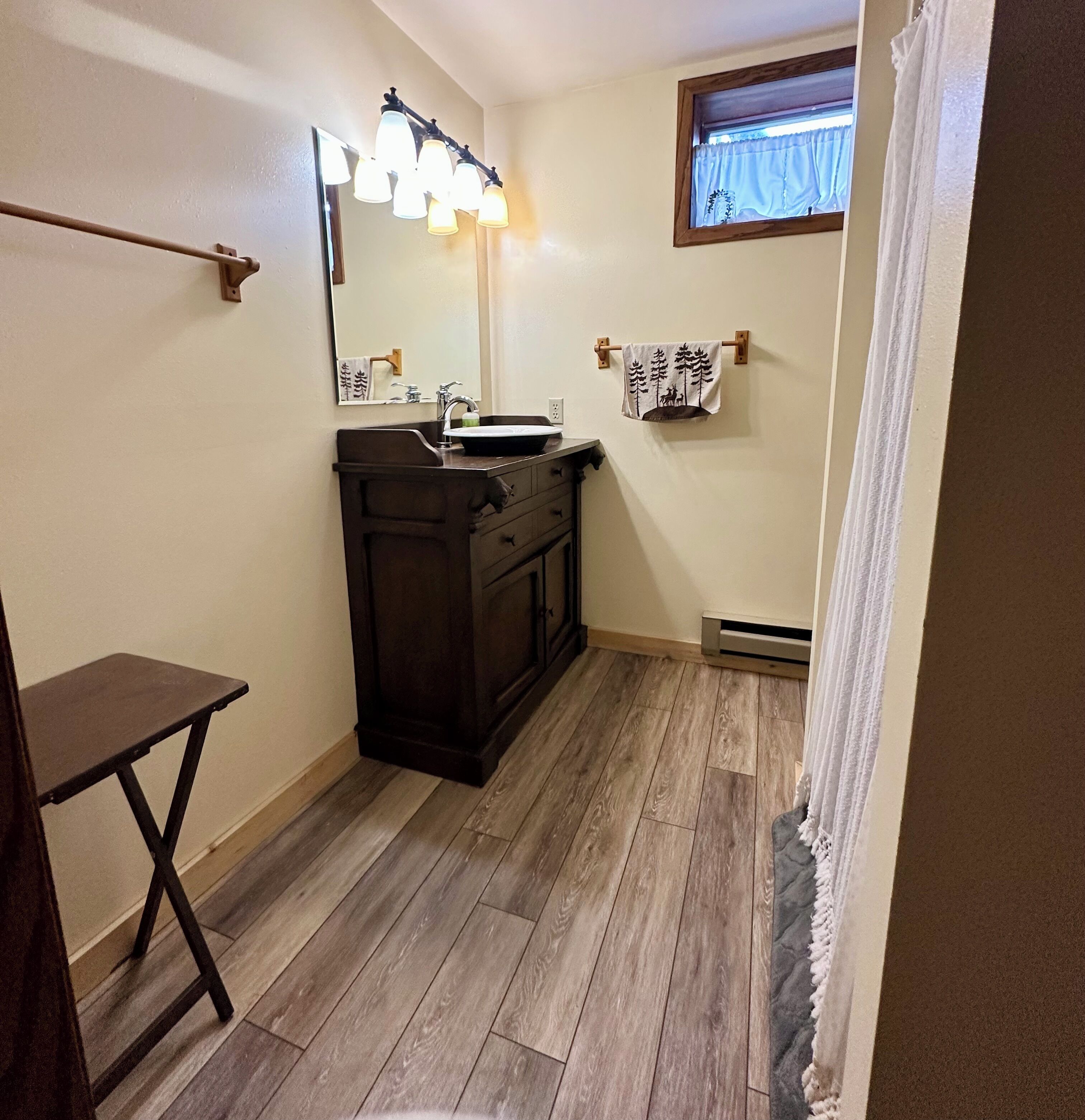 A bathroom with a dark wood vanity, a mirror with lights, a window with a curtain, and a towel rack with a patterned towel.