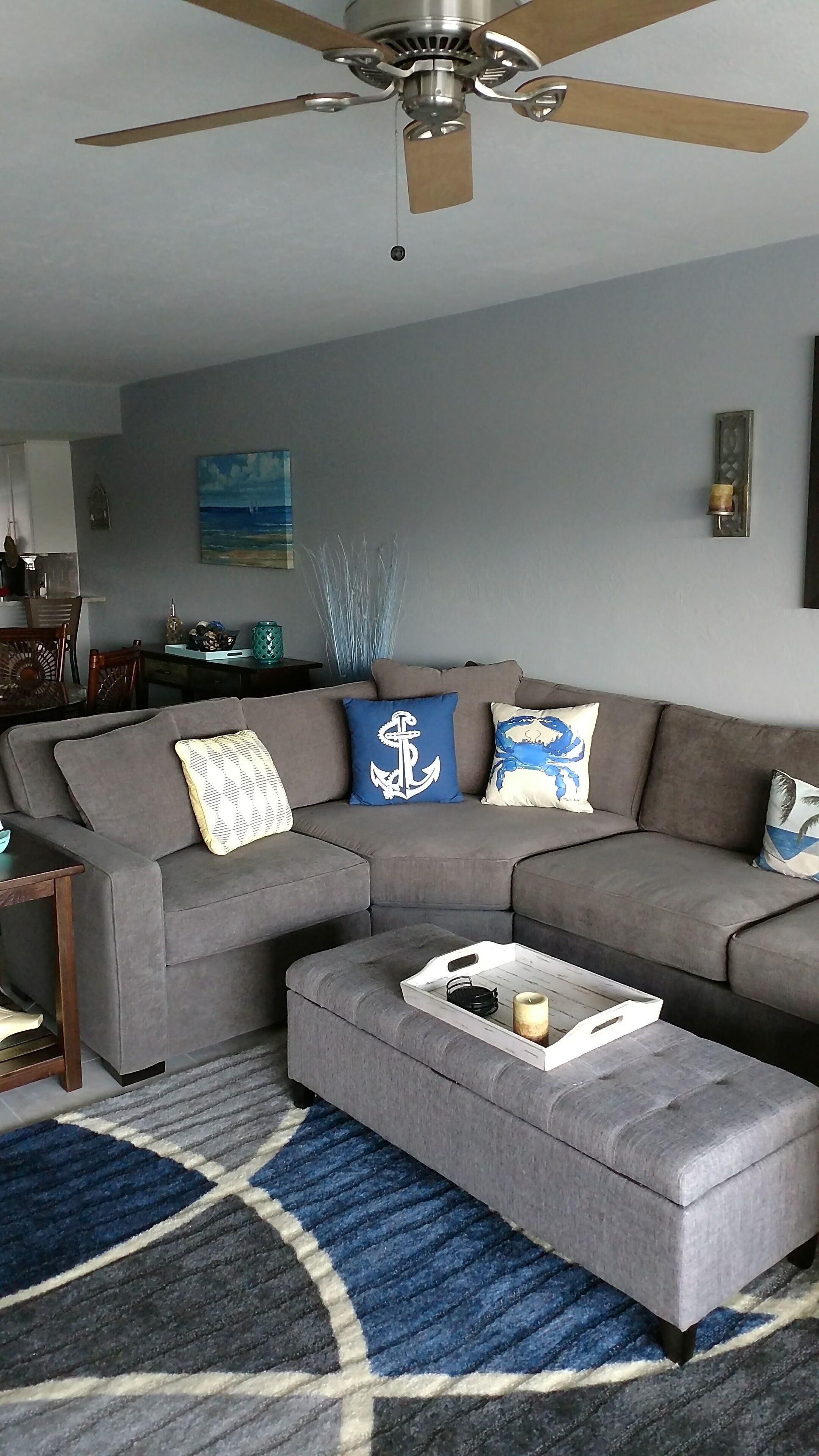 Ein Wohnzimmer mit grauem Ecksofa, einem weißen Couchtisch und einem Deckenventilator.