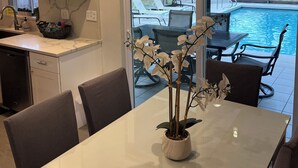 A modern kitchen with white cabinets, a dining area with a glass table, and a view of a swimming pool through large sliding doors. -  4 Bed pool House by Bay!  Lido & Siesta Key Beaches very close  (Sarasota)
