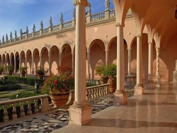 A covered courtyard with arches and columns, featuring statues and potted plants.