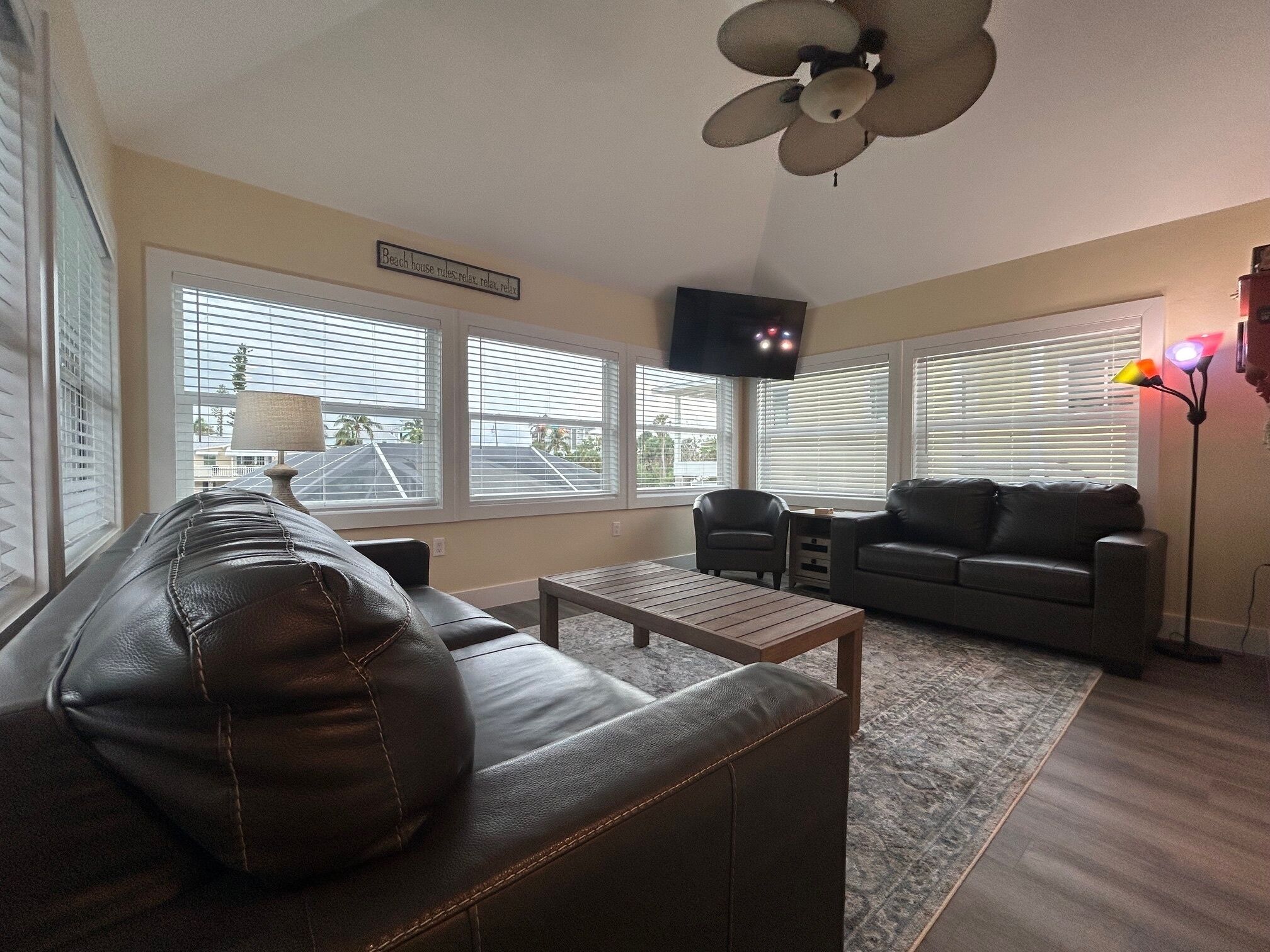 A living room with a leather sofa, a coffee table, a TV, and a ceiling fan.