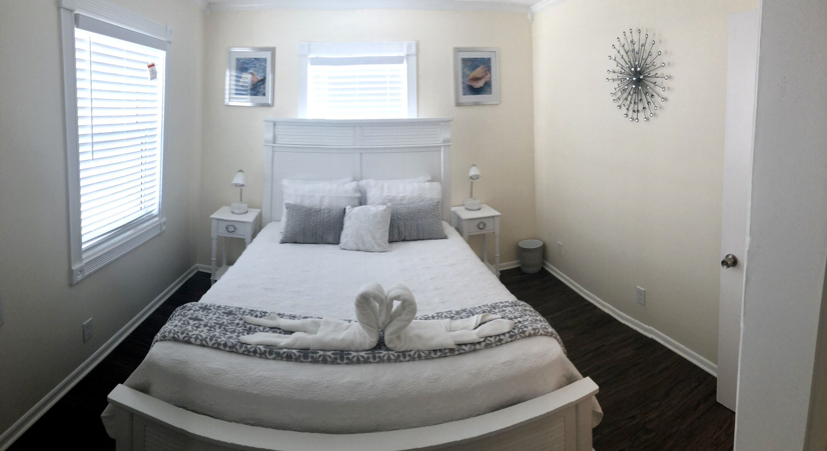 Een net opgemaakt bed met een handdoekarrangement in de vorm van een hart, een nachtkastje met een lamp en een decoratief wandobject.