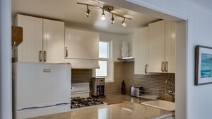 Une cuisine moderne avec des meubles blancs, un réfrigérateur en acier inoxydable, une cuisinière à gaz, un évier et une machine à café.