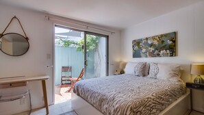 Une chambre à coucher comprenant un lit, un bureau, une chaise, une porte-fenêtre coulissante donnant sur un espace extérieur et un tableau accroché au mur.