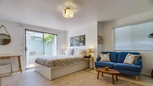 Une chambre à coucher avec un lit, un canapé bleu, une petite table et une porte-fenêtre coulissante donnant sur un patio.