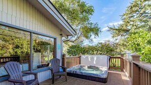 A deck with a hot tub, two Adirondack chairs, and a glass-enclosed patio area. - Beautiful Beach access/River Front Hot tub and Fire pit  (Brookings)