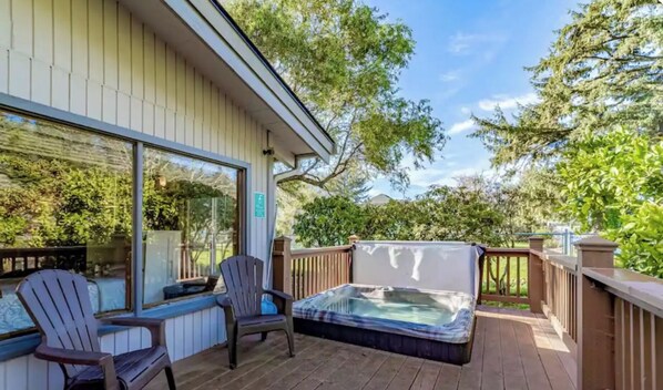 Une terrasse dotée d’un jacuzzi, de deux fauteuils Adirondack et d’un espace patio fermé par des baies vitrées.