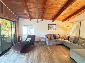 Un salon avec un plafond en bois, un canapé, un fauteuil inclinable, une petite table et une fenêtre donnant sur un paysage verdoyant.
