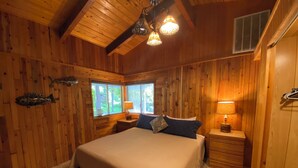 A wooden-paneled bedroom with a bed, two bedside tables, and a fish decoration. - Beautiful Beach access/River Front Hot tub and Fire pit  (Brookings)