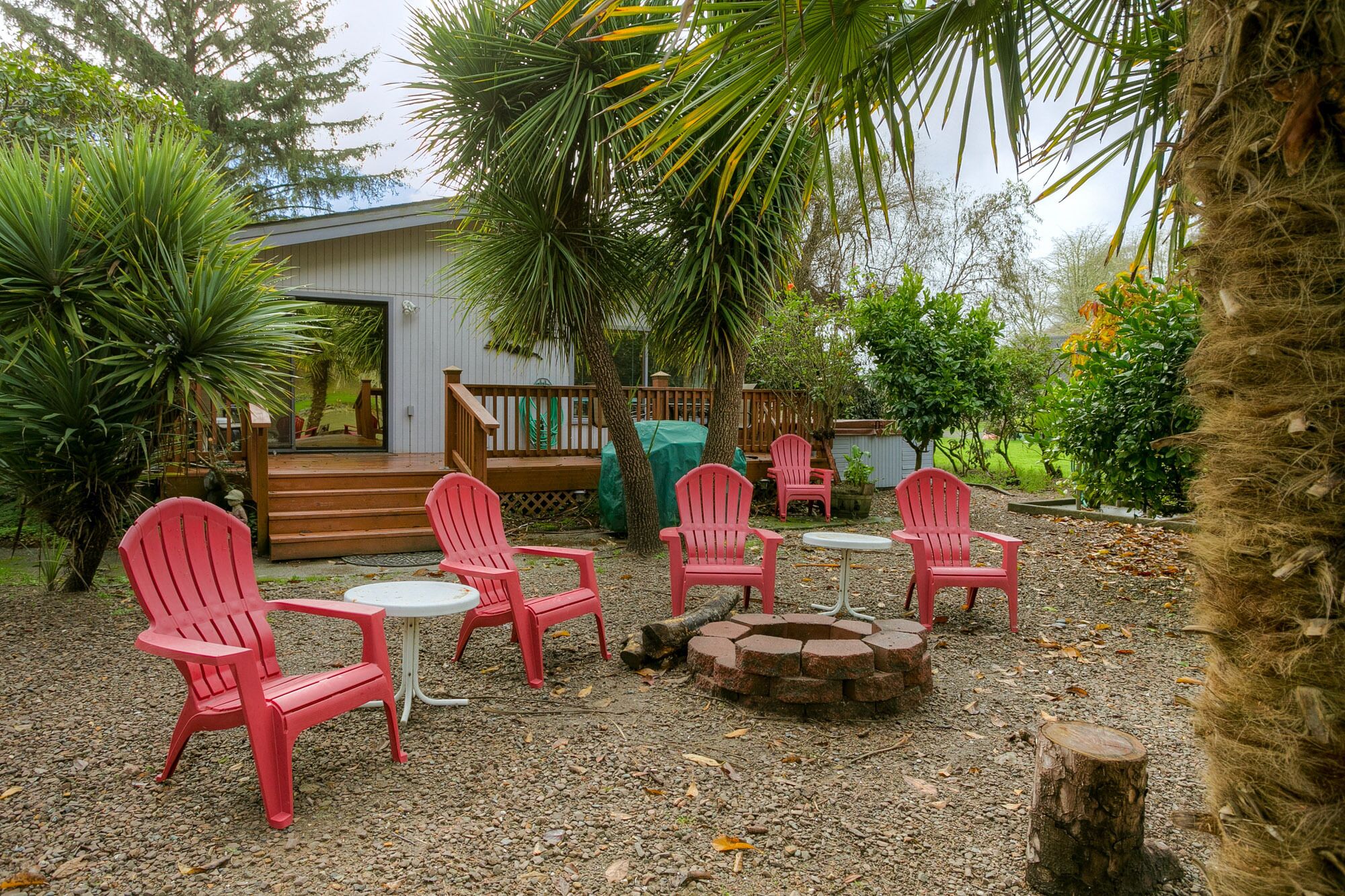A patio area with red chairs and tables, a fire pit, and surrounding greenery.