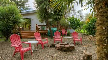A patio area with red chairs and tables, a fire pit, and surrounding greenery.