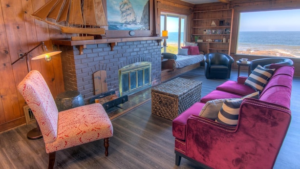 A cozy room with a fireplace, a bookshelf, a sofa, and a view of the ocean.