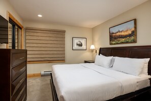 A neatly made bed with white linens, a wooden headboard, a nightstand with a lamp, a framed picture on the wall, and a wooden dresser. - Montaneros 220 - 1 Bedroom Diamond (Vail)