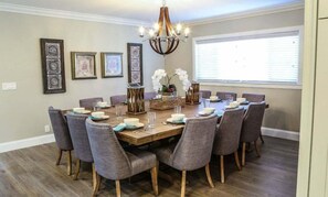 A dining room with a wooden table, grey upholstered chairs, and a chandelier.