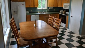 Een keuken met houten kastjes, een eettafel, stoelen, een koelkast, een vaatwasser en een magnetron.