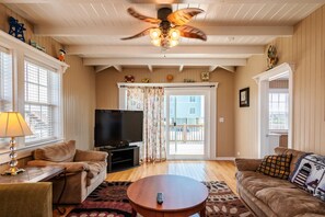 A living room with a ceiling fan, a television, two sofas, a coffee table, and a large window with curtains. - Coastal Breeze: Home Close to Beach Access and Town Park (Oak Island)