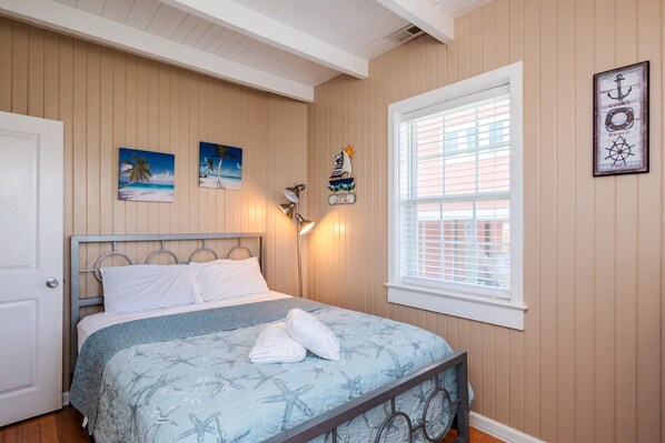 A bedroom with a bed, a window with blinds, and wall decorations including a nautical theme. - Coastal Breeze: Home Close to Beach Access and Town Park (Oak Island)