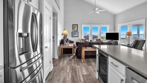 A modern kitchen with a large stainless steel refrigerator, wooden flooring, and a dining area with a table and chairs. - Spinnaker: Oceanfront Home with Expansive Views (Oak Island)