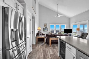 A modern kitchen with a large stainless steel refrigerator, wooden flooring, and a dining area with a table and chairs. - Spinnaker: Oceanfront Home with Expansive Views (Oak Island)