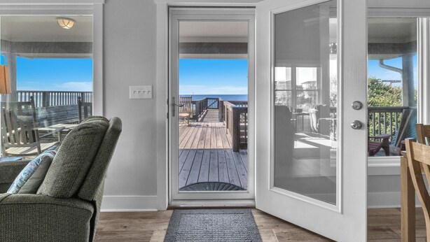 A room with a door leading to a wooden deck with a view of the ocean. - Spinnaker: Oceanfront Home with Expansive Views (Oak Island)