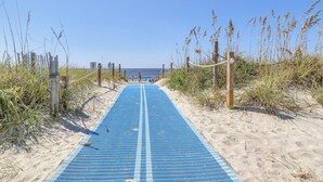 A sandy beach path with a blue mat leading to the sea, surrounded by tall grasses and wooden posts. - Spinnaker: Oceanfront Home with Expansive Views (Oak Island)