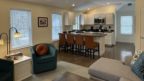 A modern kitchen with white cabinets, a microwave, and a stove. There is a dining area with a table and chairs, and a ceiling fan above. - Falmouth Waterfront Carriage House Apt (Falmouth)