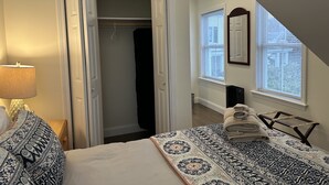 A bedroom with a bed, a bedside lamp, a closet, a window with blinds, and a towel rack. - Falmouth Waterfront Carriage House Apt (Falmouth)