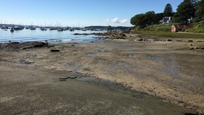 A coastal beach with rocky terrain, a small red building, and a marina with boats. - Falmouth Waterfront Carriage House Apt (Falmouth)