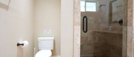 Une salle de bain comprenant des toilettes, une douche avec une porte en verre et un porte-serviettes.