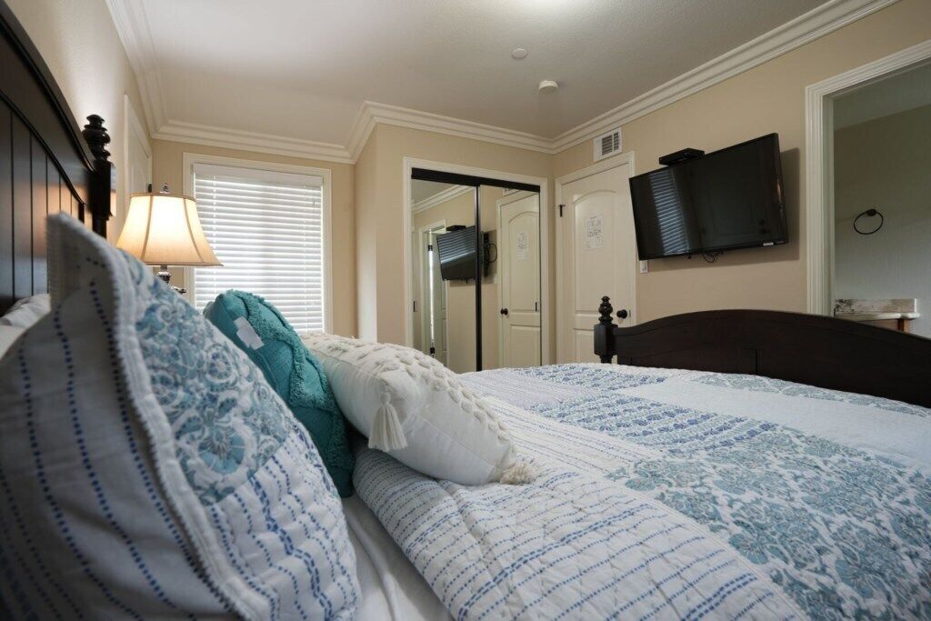 Un dormitorio con una cama, un televisor montado en la pared y una puerta que da a otra habitación.