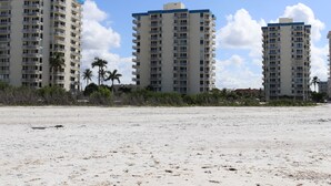Un hotel frente a la playa con varios edificios altos, una playa de arena y palmeras.