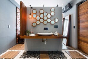 Un baño moderno con un lavamanos grande, espejos hexagonales y un mueble de tocador de madera.
